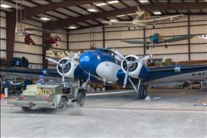 A man steers a vehicle backwards towing a small airplane in a hangar